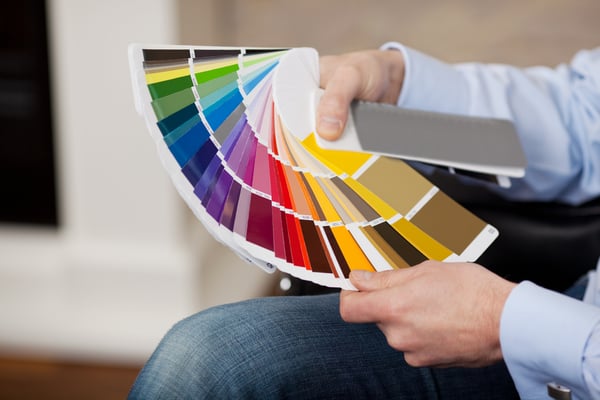 Man holding a set of paint color swatches in all the colors of the spectrum splayed out in his hand as he tries to decide on a new color for his house